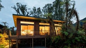 Una casa moderna con terraza de madera, ventanas amplias y vistas a árboles y montañas circundantes.