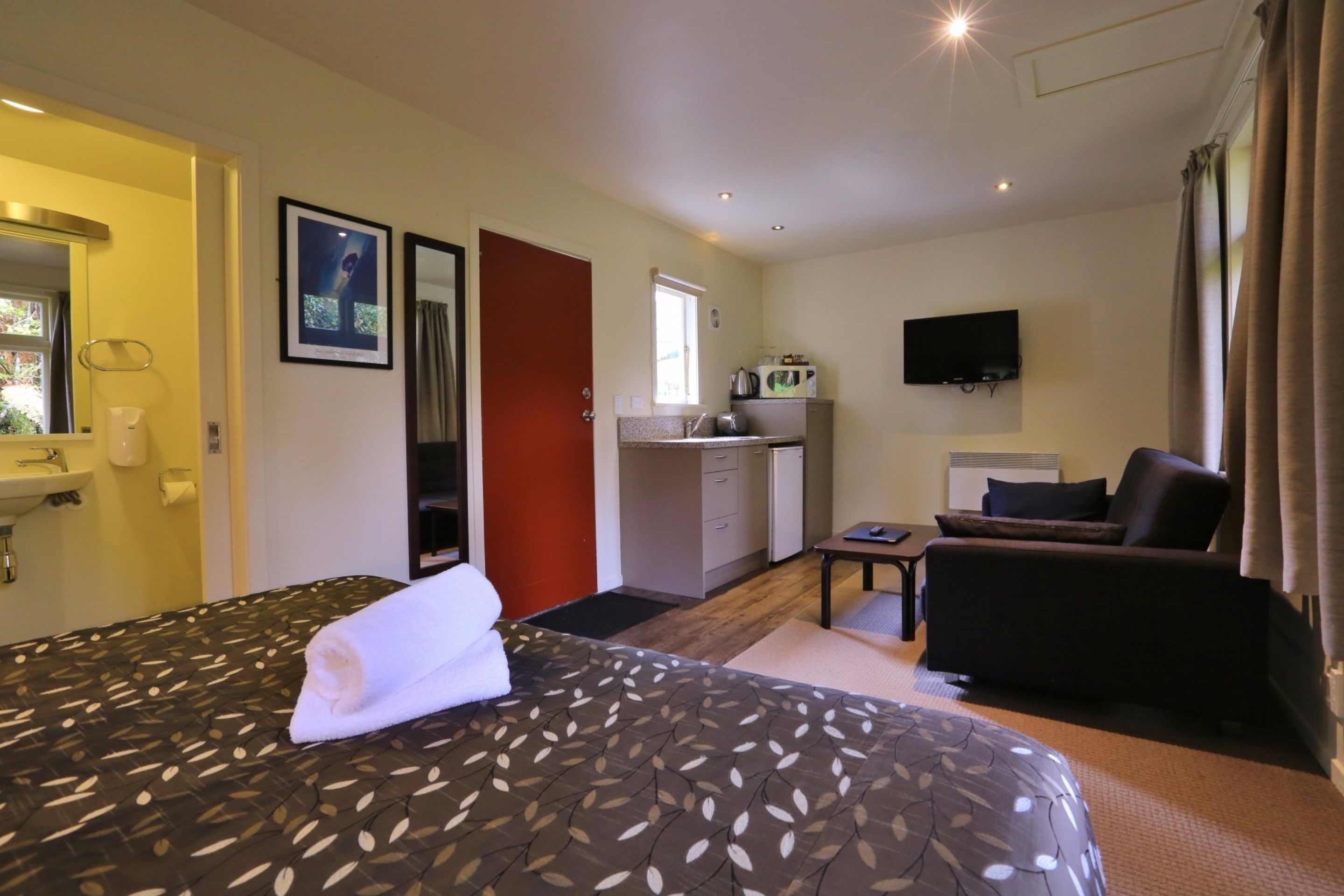 Une chambre d’hôtel équipée d’un lit, d’un bureau, d’une chaise, d’une télévision et d’une kitchenette.