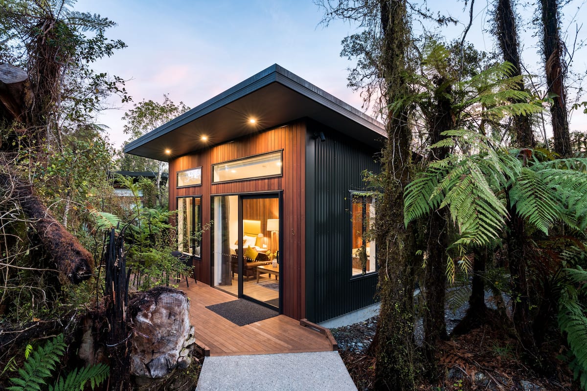 Una casa moderna con terraza de madera, ventanas grandes y vistas al bosque circundante.