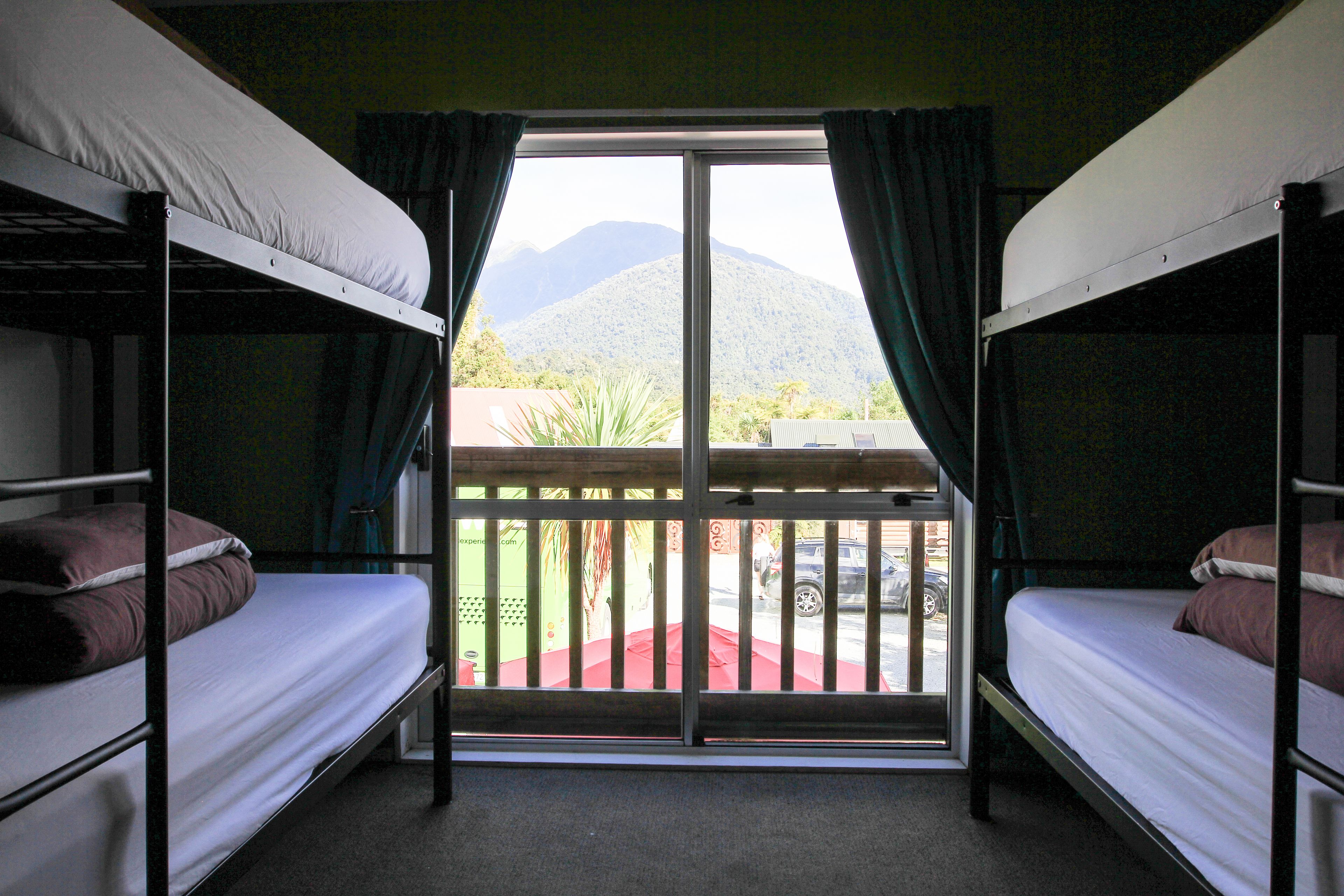 A room with bunk beds, a sliding glass door leading to an outdoor area with a view of mountains.