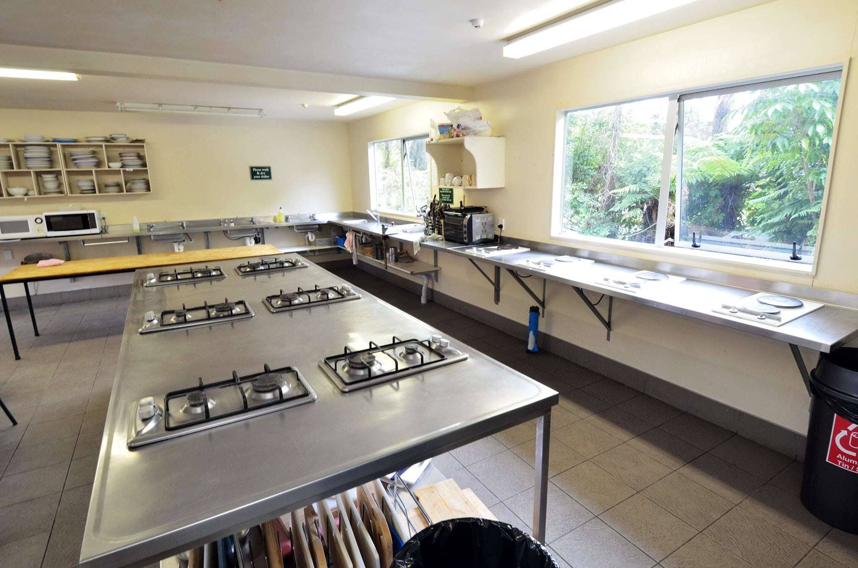 A kitchen with four gas stoves, a microwave, and a window with a view of greenery.