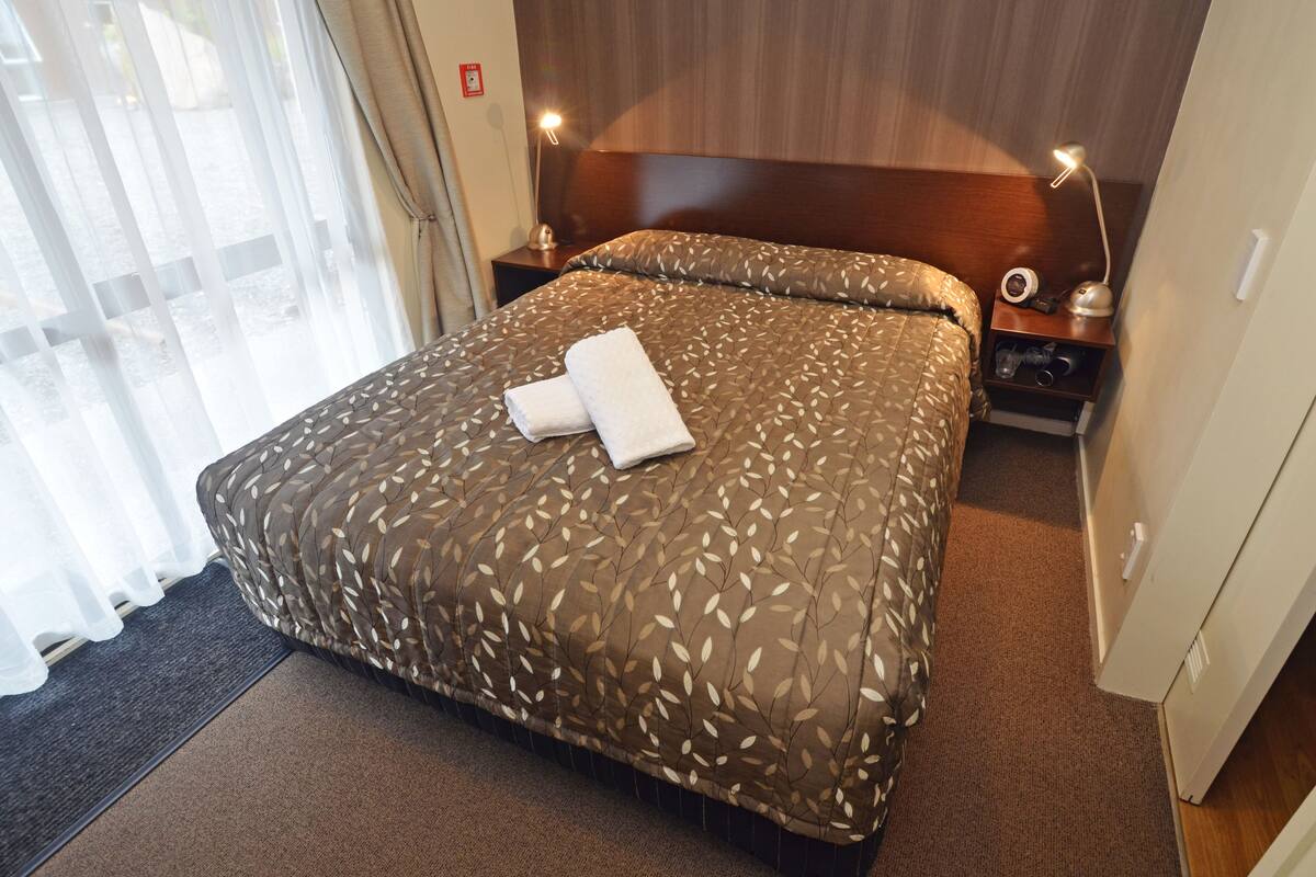 Una habitación de hotel con una cama, una mesita de noche, una lámpara y una puerta.