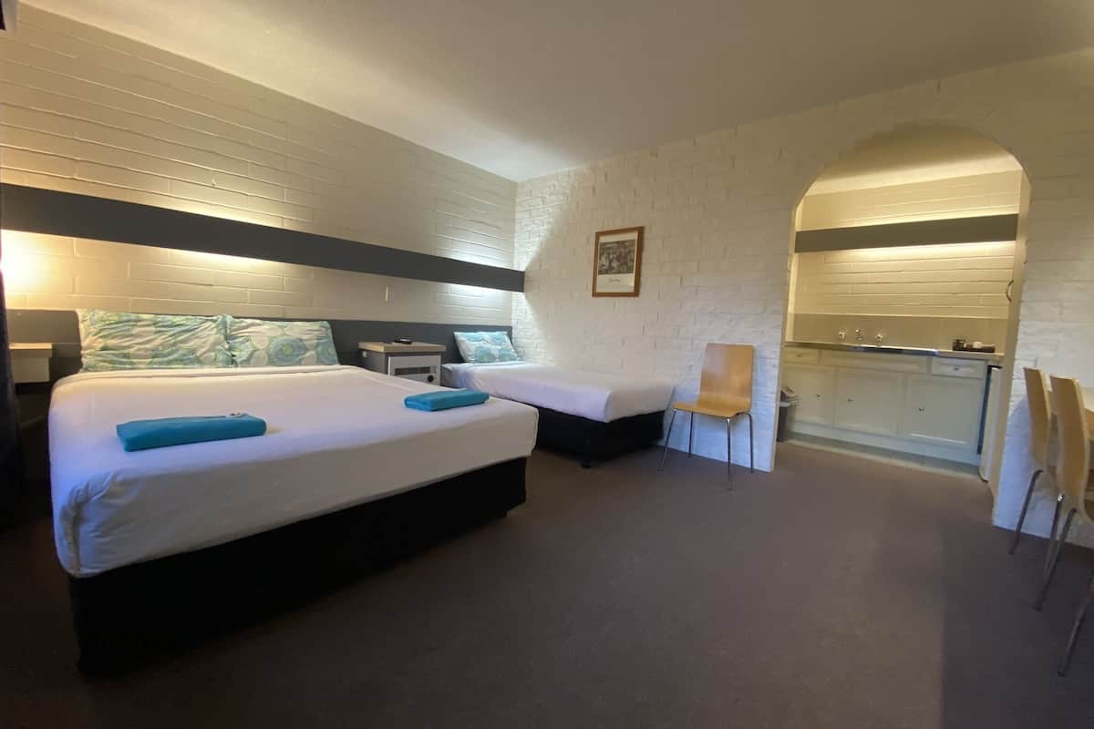 A hotel room with two beds, a desk, a chair, and a kitchenette.