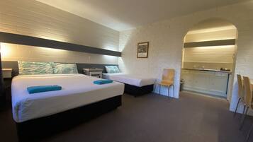 A hotel room with two beds, a desk, a chair, and a kitchenette.