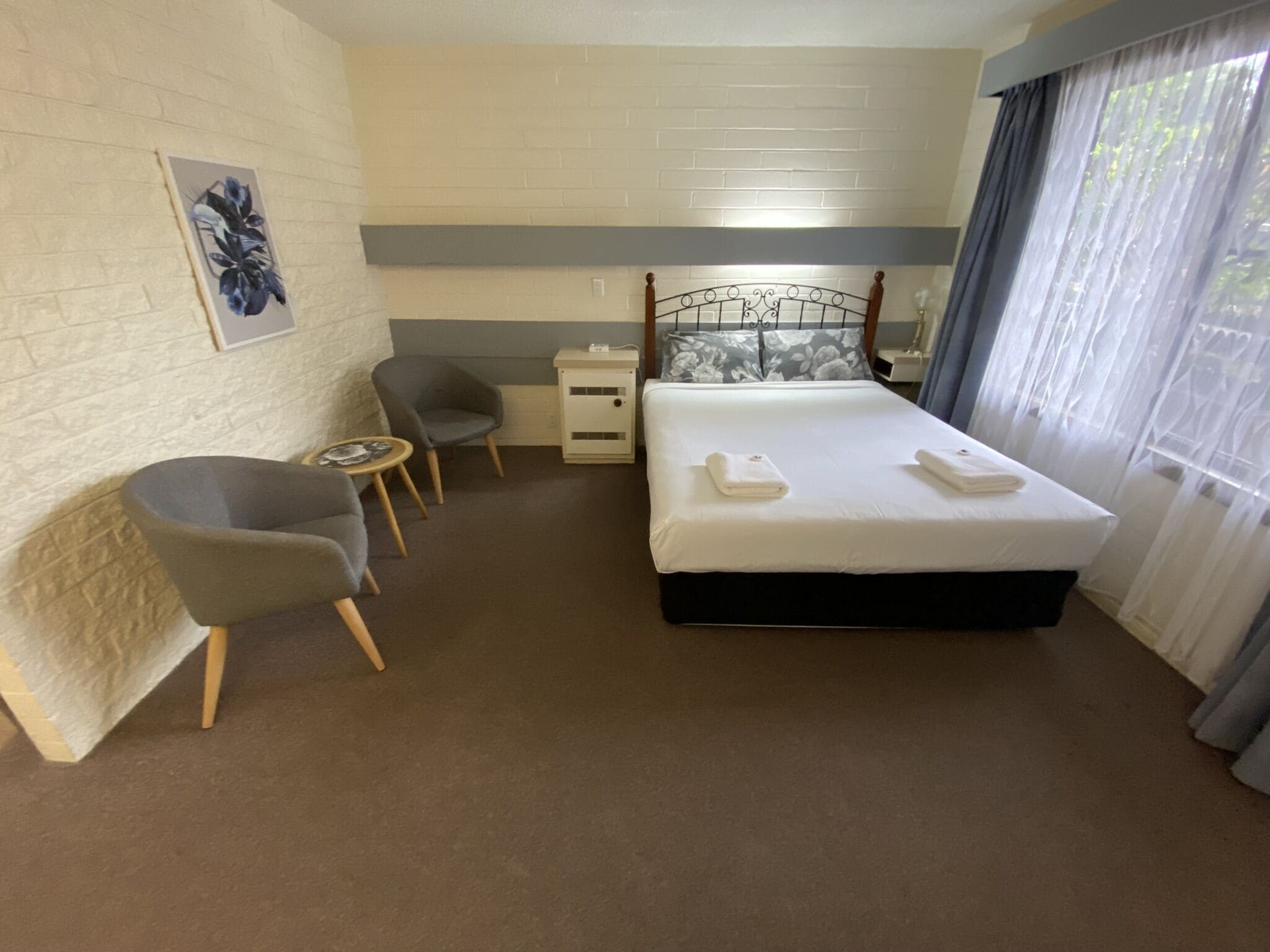 Habitación de hotel con cama, una silla, una mesita pequeña, una mesita de noche y una ventana con cortinas.