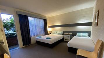 Quarto de hotel com duas camas, uma escrivaninha, uma cadeira e uma janela com cortinas.
