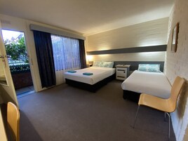 Una habitación de hotel con dos camas, un escritorio, una silla y un ventanal con cortinas.