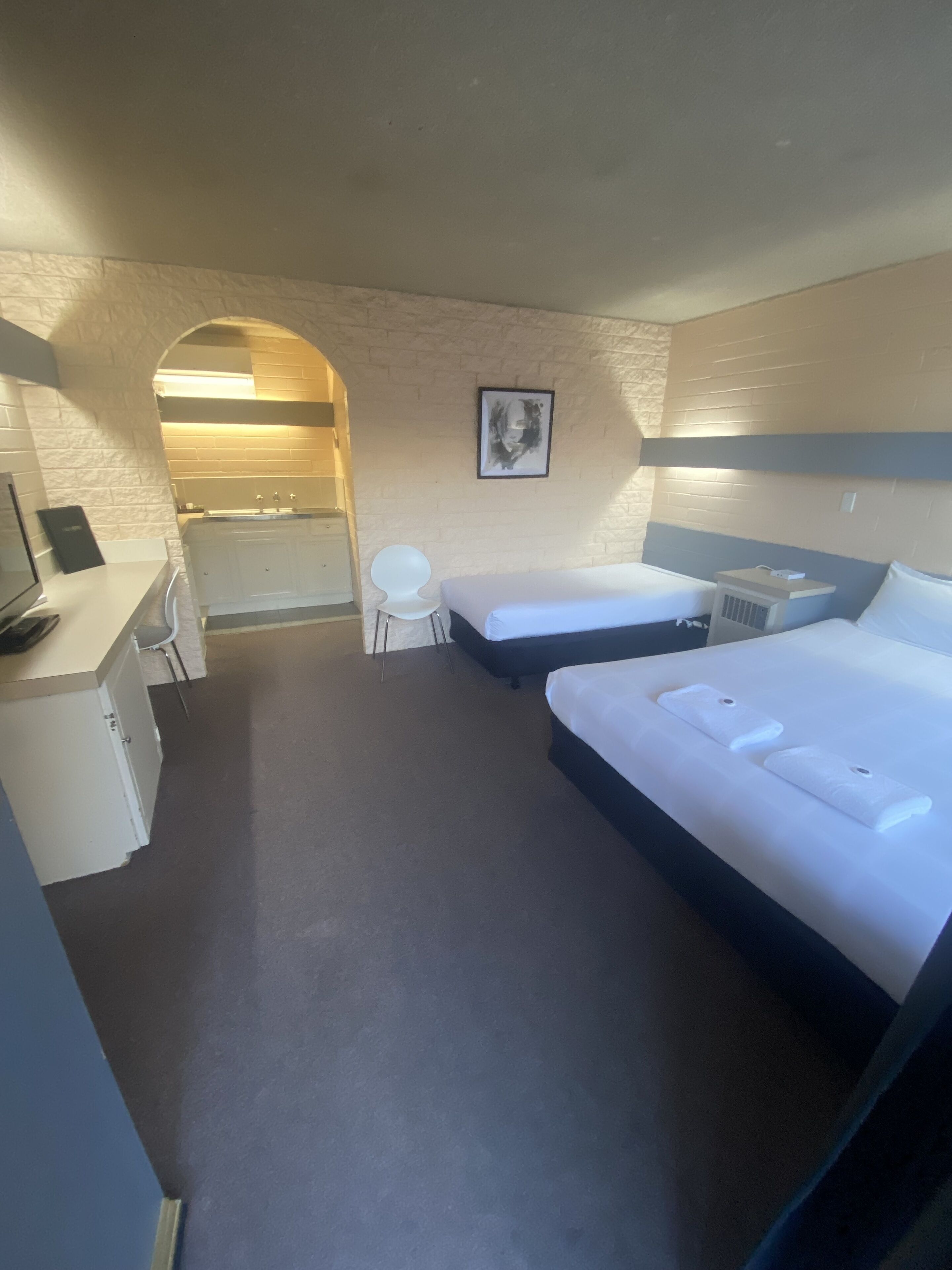 A hotel room with two beds, a desk, a chair, and a bathroom visible through an archway.