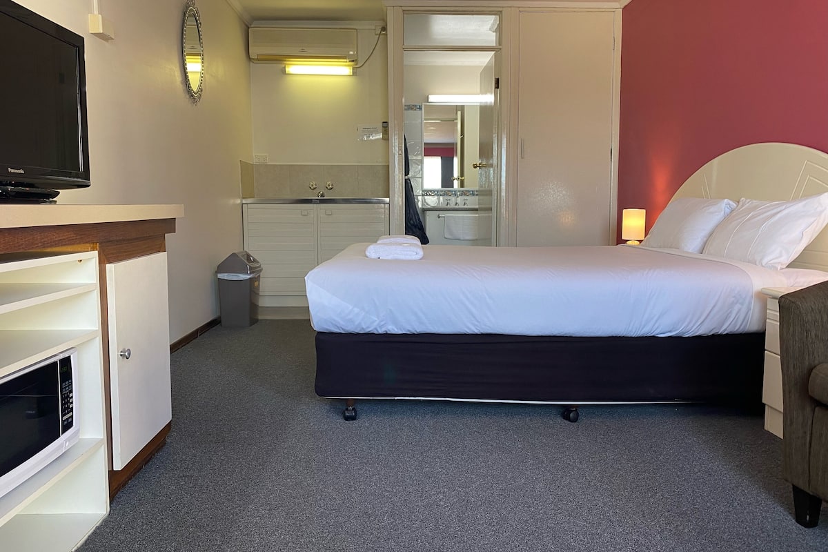 A hotel room with a bed, a television, a desk, a mirror, and a bathroom visible through an open door.