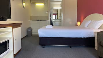 A hotel room with a bed, a television, a desk, a mirror, and a bathroom visible through an open door.