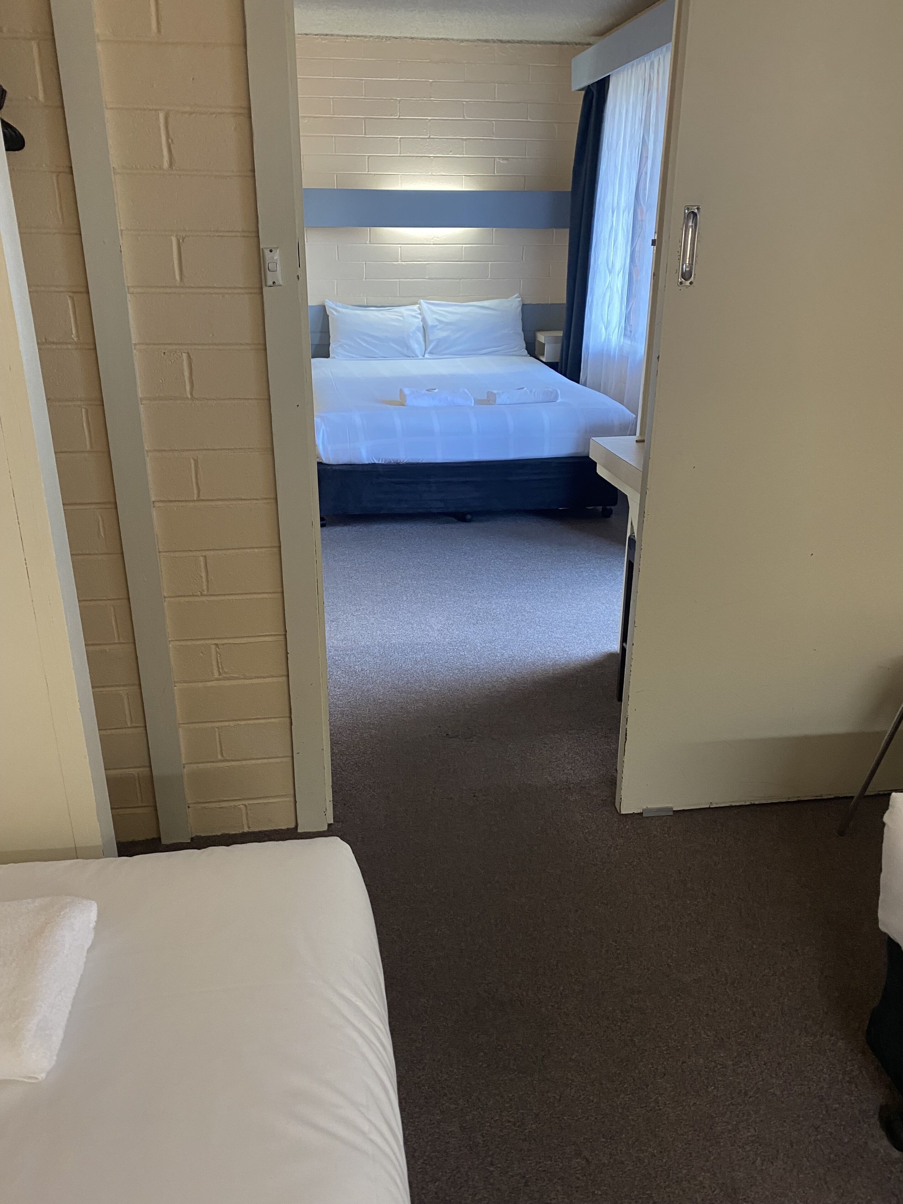 A hotel room with a bed, a small table, and a window with curtains.