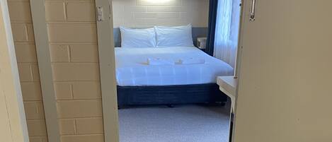 A hotel room with a bed, a small table, and a window with curtains.