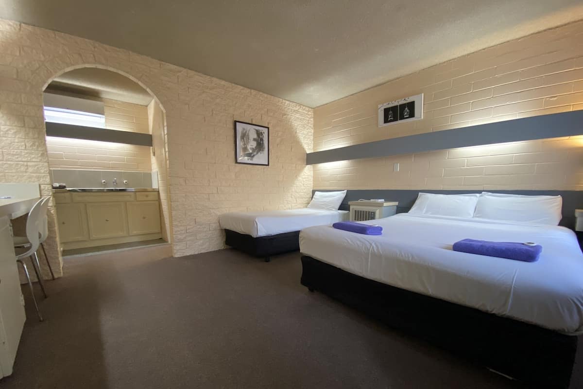 A hotel room with two beds, a desk, and a kitchenette.