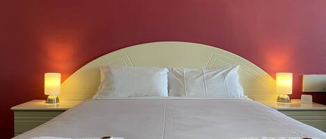 A neatly made bed with white linens and pillows, two bedside lamps, and two white towels on the bed.