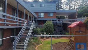 Un immeuble à plusieurs étages, doté d’une façade en briques, d’un espace extérieur couvert et d’une aire de jeux avec un toboggan et une structure d’escalade.