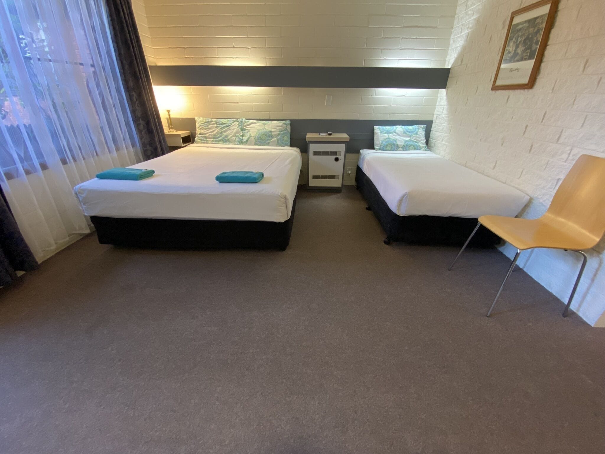 A hotel room with two beds, a chair, a nightstand, and a window with curtains.