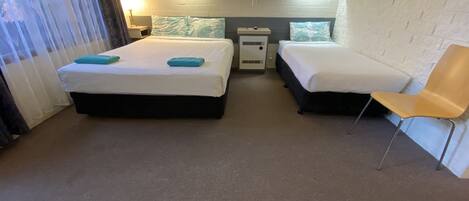 A hotel room with two beds, a chair, a nightstand, and a window with curtains.