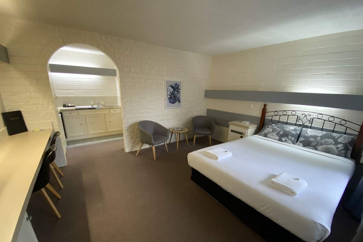A hotel room with a bed, a desk, a chair, a small table, and a kitchenette.
