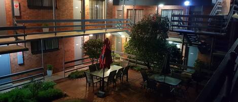 Un patio al aire libre de varios niveles con mesas y sillas, rodeado de muros de ladrillo y plantas en macetas.