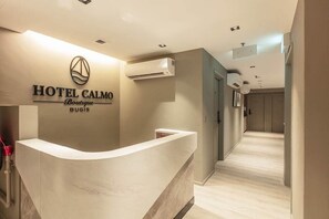 A hotel reception area with a marble counter, a logo above the reception desk, and an air conditioning unit on the wall. - Beach Hotel (Singapore)