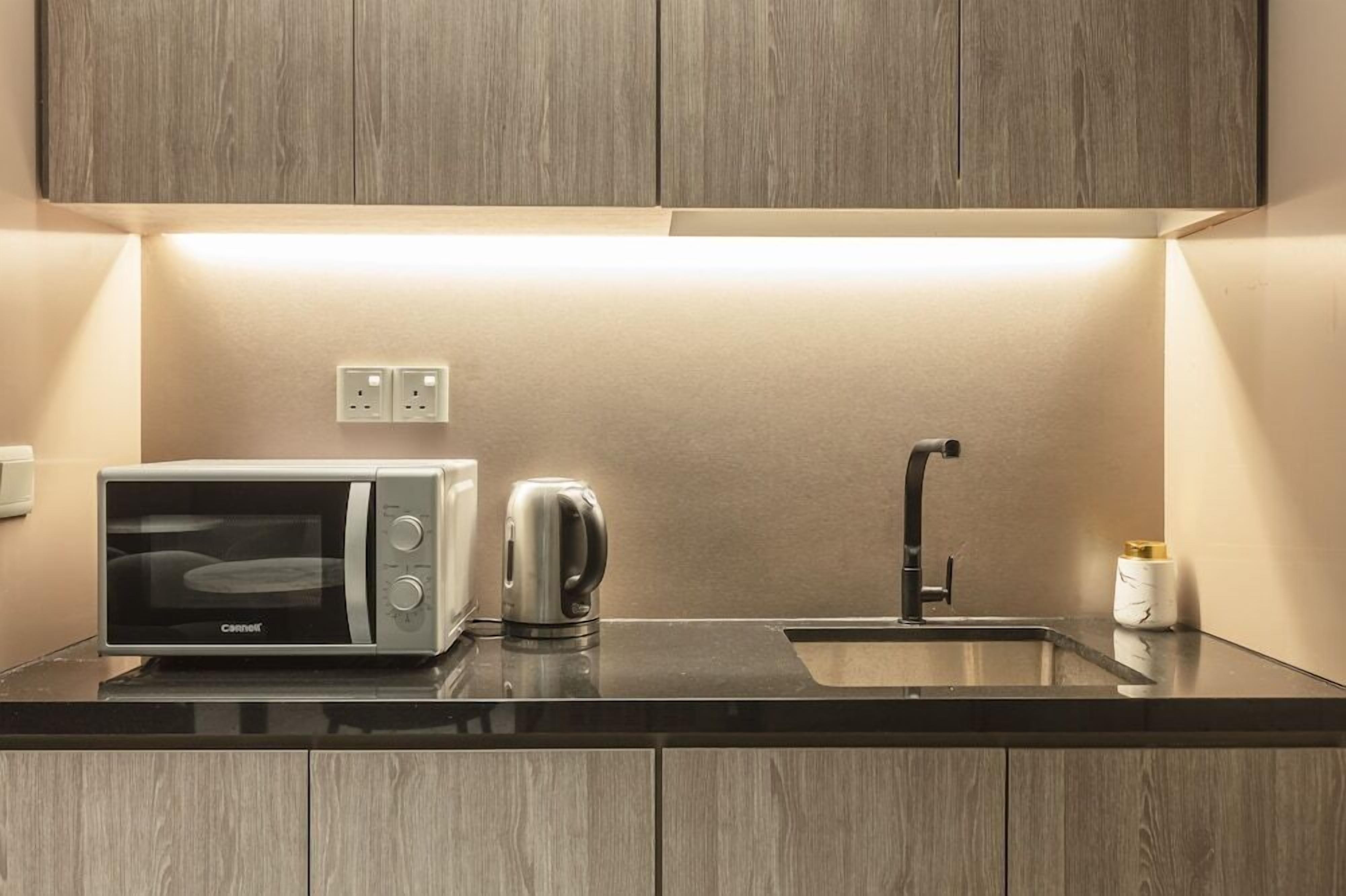 A kitchen with a microwave, kettle, sink, and wooden cabinets.