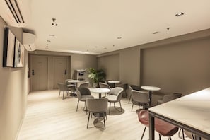 A modern hotel room with a dining area featuring round tables and chairs, a large window, and a plant. - Beach Hotel (Singapore)