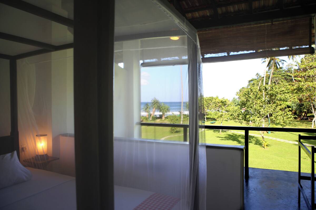 Een kamer met een bed, een raam met uitzicht op de oceaan en een balkon met een leuning.