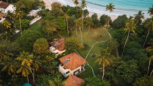 Vista aérea de una propiedad costera con varias casas, una playa y densa vegetación tropical.