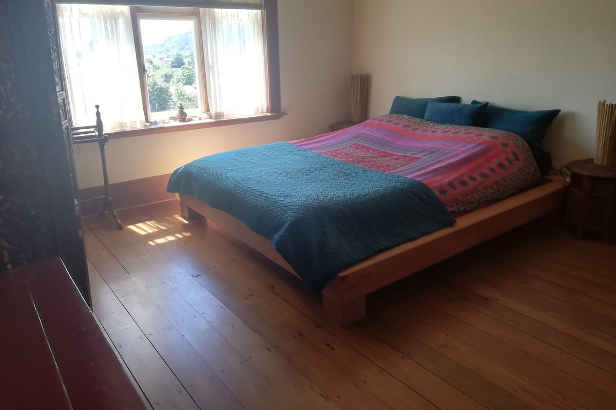 Ein Schlafzimmer mit einem hölzernen Bett, einem Fenster mit Vorhängen und einem Nachttisch.
