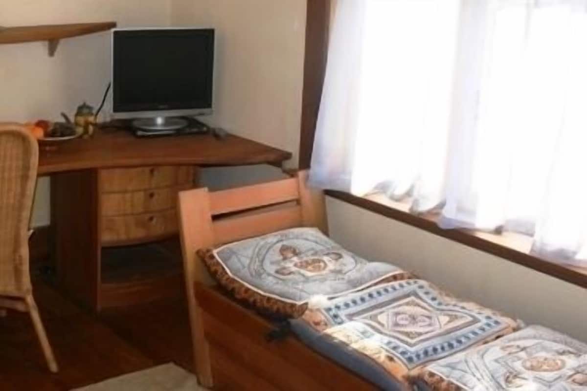 Ein kleines Zimmer mit Schreibtisch, Stuhl und Bett.