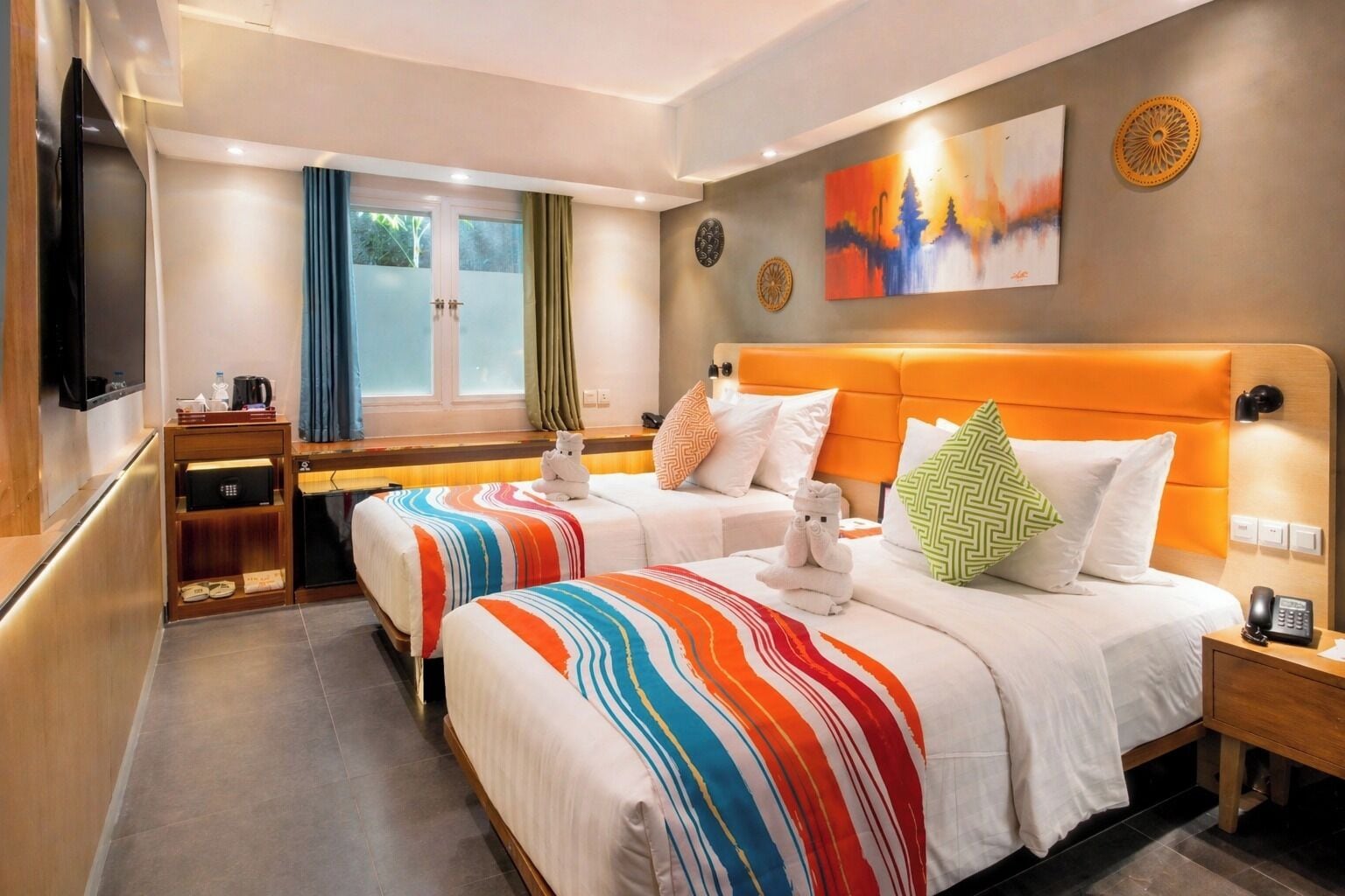 Habitación de hotel con dos camas, televisión, escritorio y ventana con cortinas.