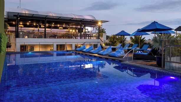 A swimming pool with lounge chairs and umbrellas, a covered seating area, and a bar. - J4 Hotels Legian (Kuta)