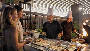 A buffet setup with various food items and a chef preparing food. - J4 Hotels Legian (Kuta)
