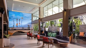 A spacious lobby with a large digital screen, comfortable seating areas, and a view of the outdoors through large windows. - J4 Hotels Legian (Kuta)