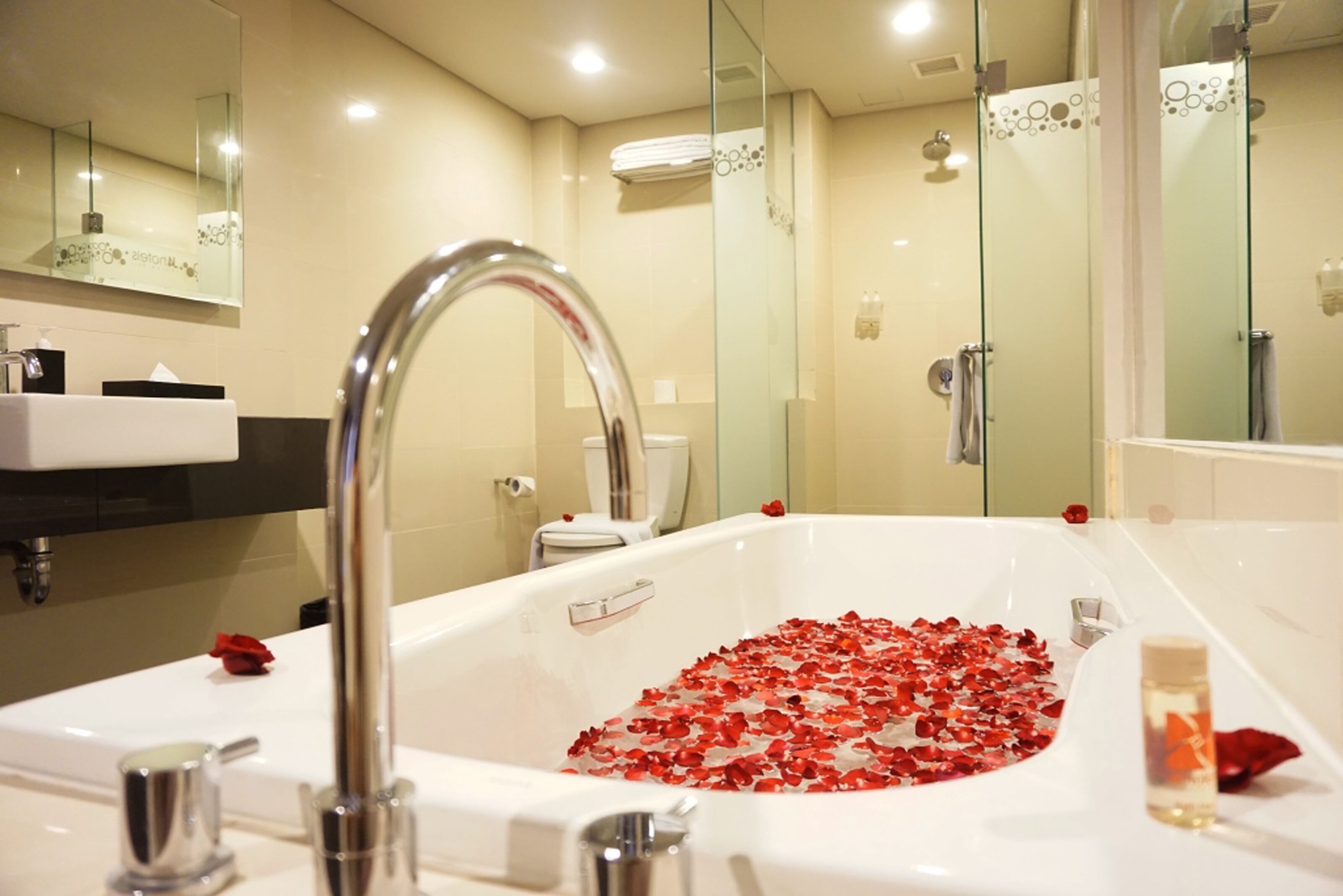 Une salle de bain avec une baignoire remplie de pétales de rose, un grand miroir et une cabine de douche en verre.