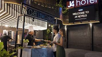 A chef serving food at a live cooking station with a sign for J4 hotel and a welcome sign.