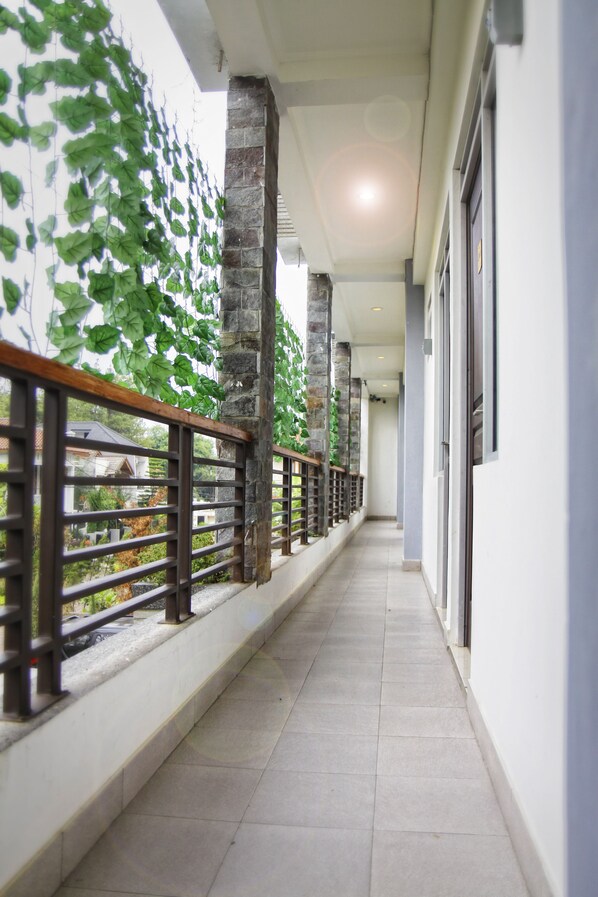 A corridor with a stone pillar, a wooden railing, and a view of a house through the railing. - Lotus Bandung (Bandung)