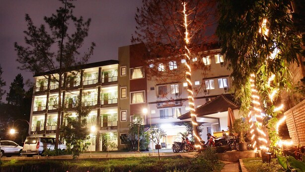 Un hôtel à plusieurs étages doté de balcons, d’une entrée couverte et d’un parking où sont stationnées des voitures et des motos.