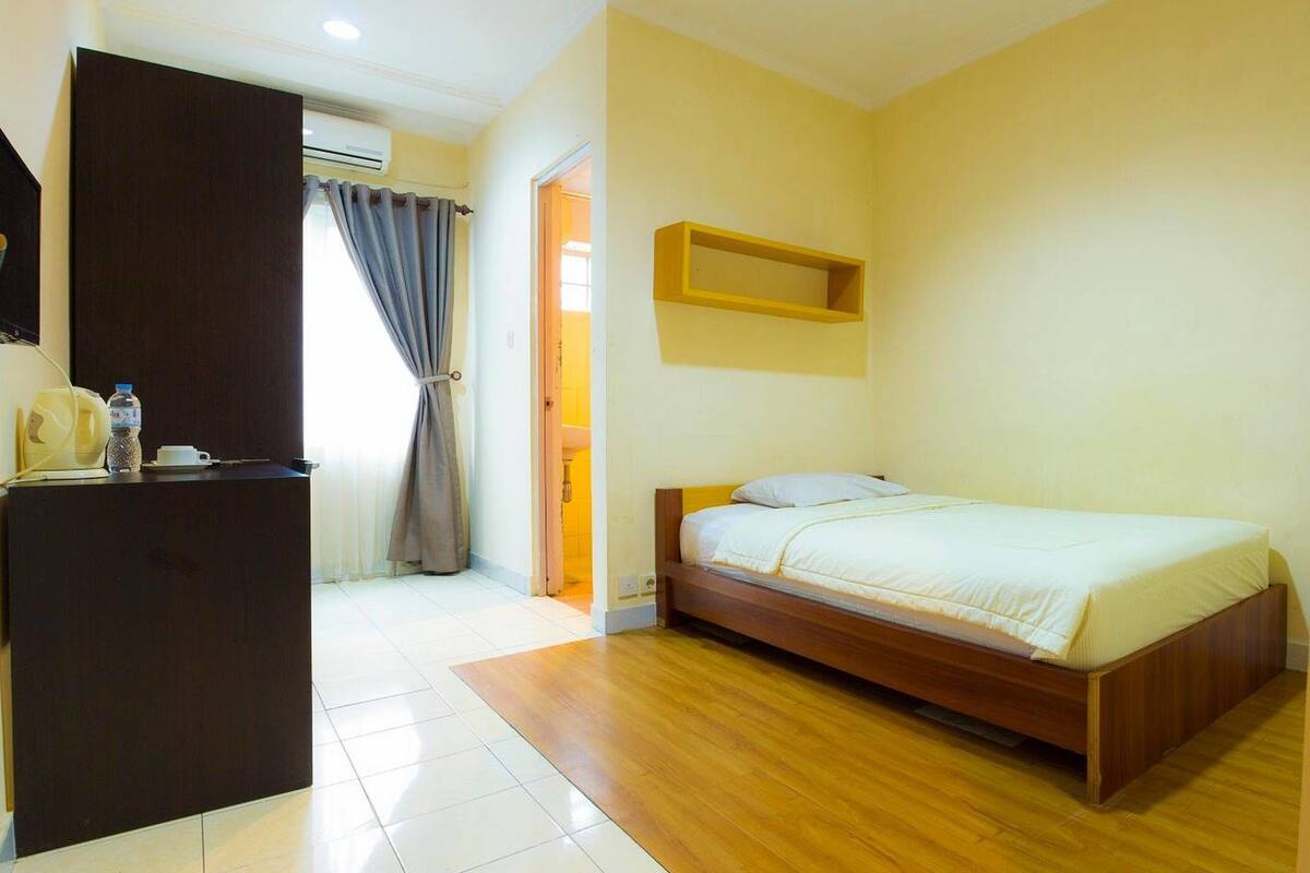 A bedroom with a wooden bed, a desk with a water bottle, a mirror, and a shelf.
