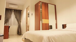 Une chambre d’hôtel équipée d’un lit, d’une armoire, d’un miroir, d’une fenêtre avec des rideaux et d’un appareil de climatisation.