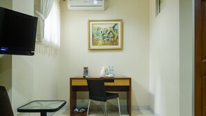 Une petite pièce avec un bureau en bois, une chaise noire, un téléviseur, un tableau accroché au mur et une petite table avec une chaise.
