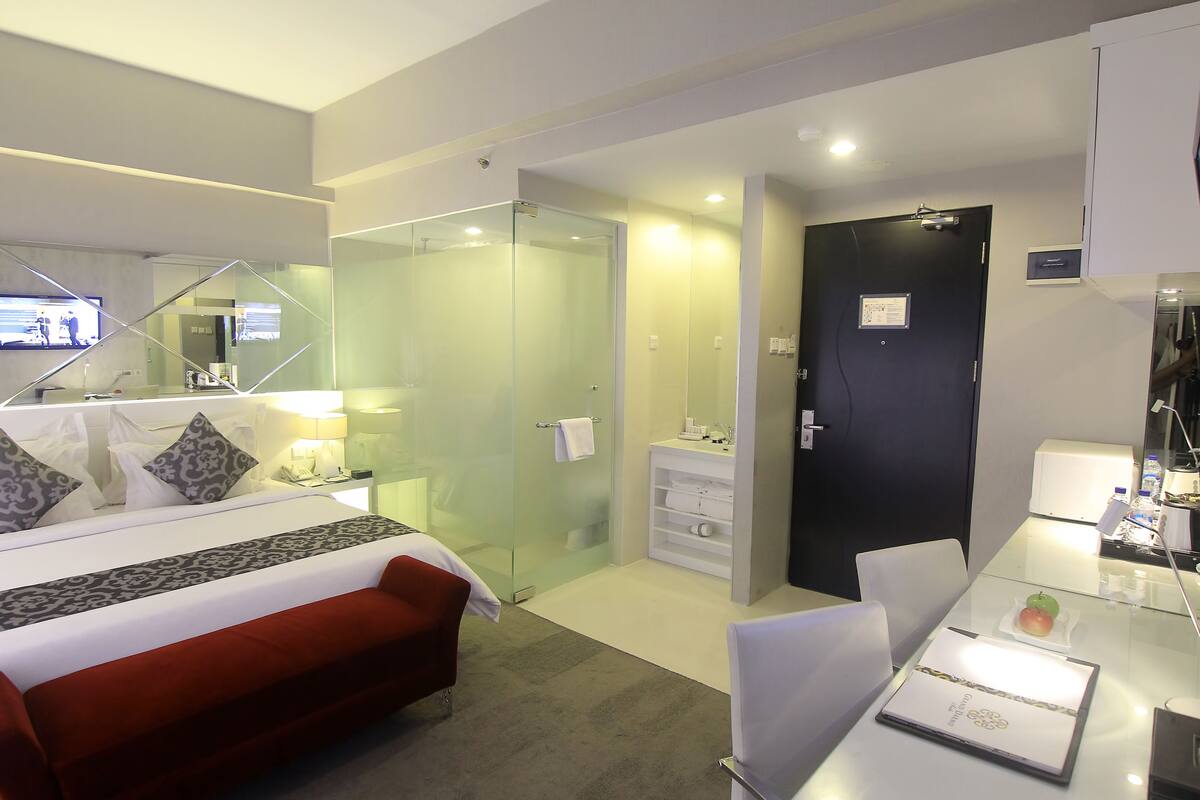 Habitación de hotel moderna con cama, escritorio, silla, cabina de ducha de vidrio y una puerta.