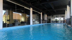 Una piscina interior con paredes de vidrio transparente, zonas de estar visibles y vistas del edificio exterior.