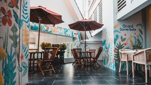 Un comedor con sillas y mesas de madera, un mural con hojas tropicales y un letrero que dice "Grand Darma Suite".