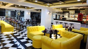 Un vestíbulo de hotel con sofás amarillos, piso de cuadros y una zona de bar con un teléfono rojo.