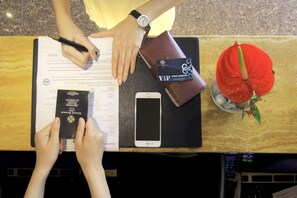 Una persona sostiene un pasaporte y una tarjeta de visa sobre una mesa con un teléfono inteligente, una cartera y una flor roja.