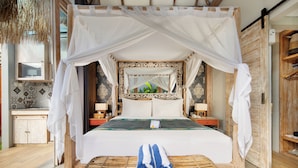 A bed with a canopy, a bedside table, a nightstand, and a wicker chair. - 18 Suite Villa Kuta (Kuta)