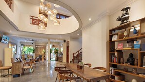 A spacious dining area with a long wooden table and chairs, a bookshelf with various items, and a ceiling with hanging lights. - 18 Suite Villa Kuta (Kuta)