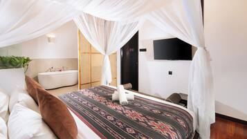 A bedroom with a bed, a white canopy, a TV on the wall, and a bathroom with a bathtub.