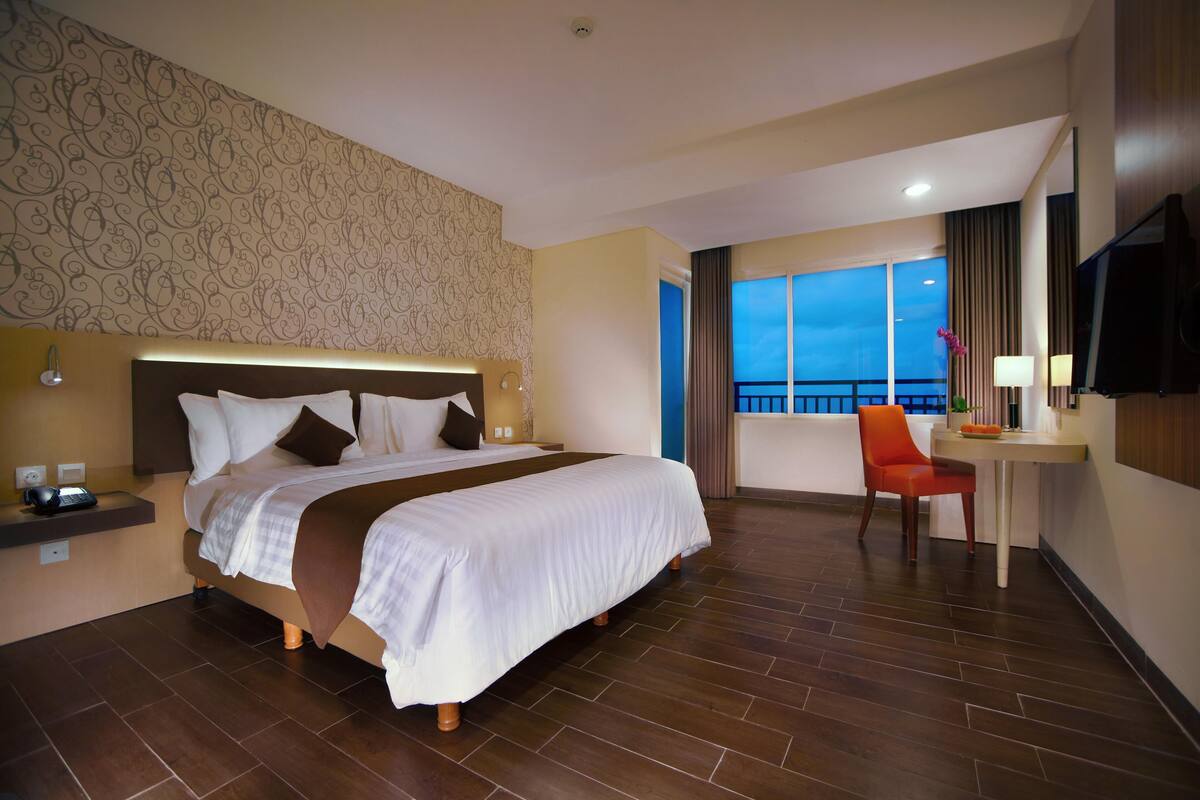 Une chambre d’hôtel avec un grand lit, un bureau avec une chaise, une télévision et un balcon avec vue.